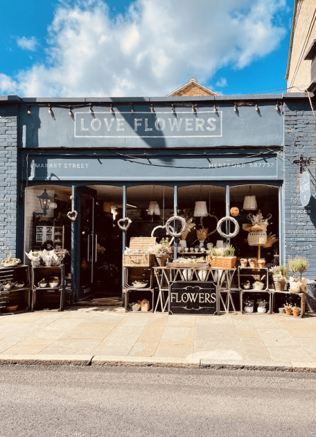 A shop selling flowers across the street with a sign saying "love flowers"