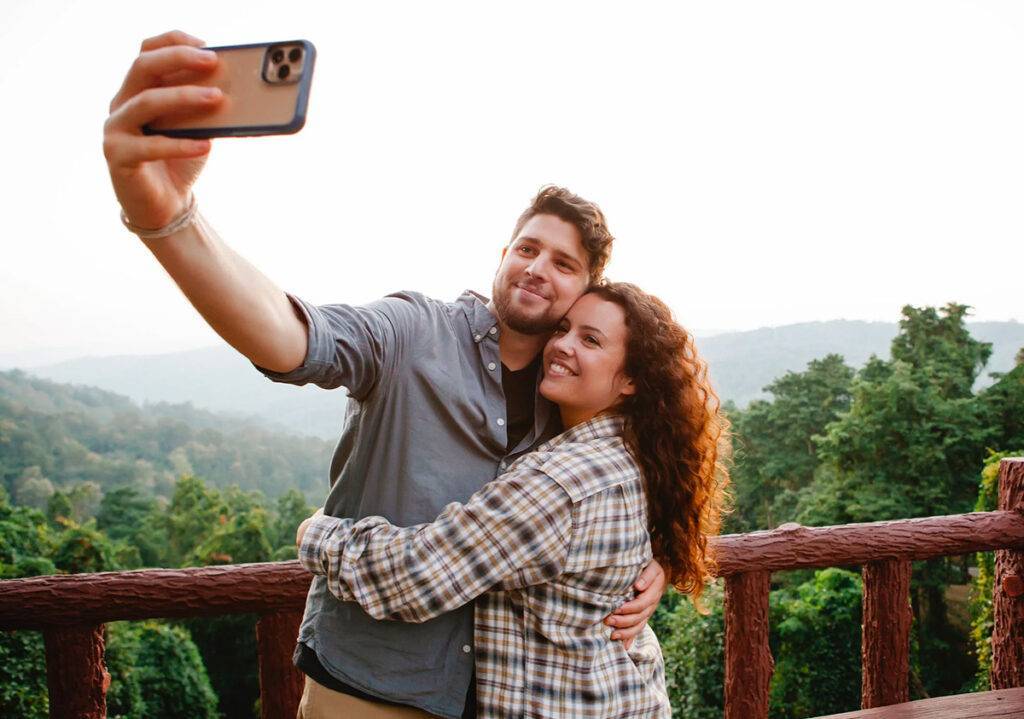 Two people hugging and taking a selfie in front of a forest